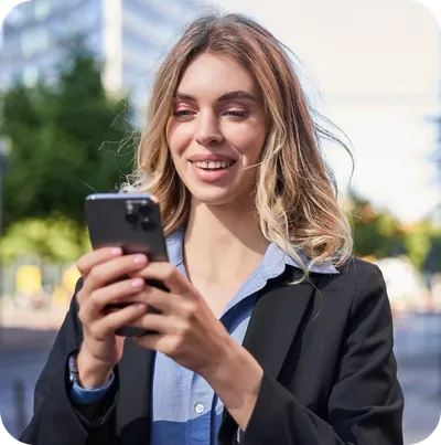 Vertical shot of curly haired woman uses mobile phone browses websites spends free time on social networks wears casual clothes stands against modern city building technology and lifestyle